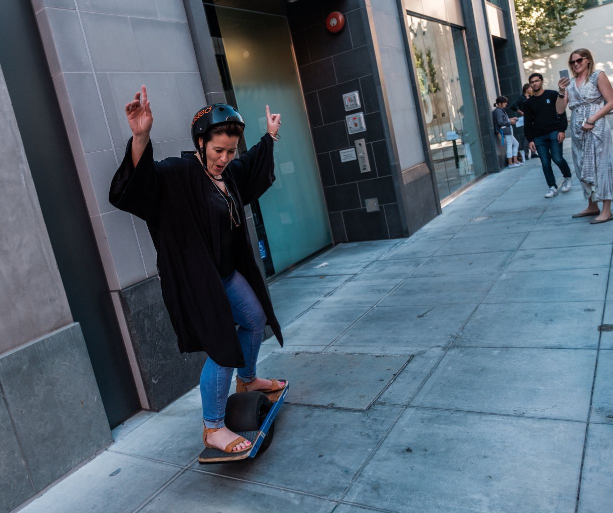 Woman is skateboarding down the sidewalk as people look on.