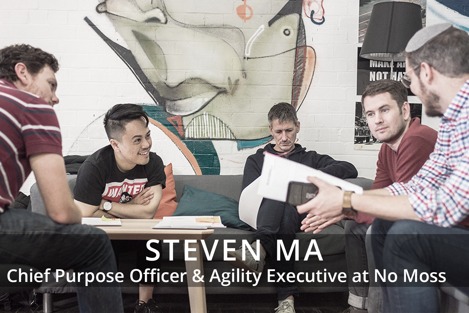 Female participants in a workshop sit in front of a graffiti wall.