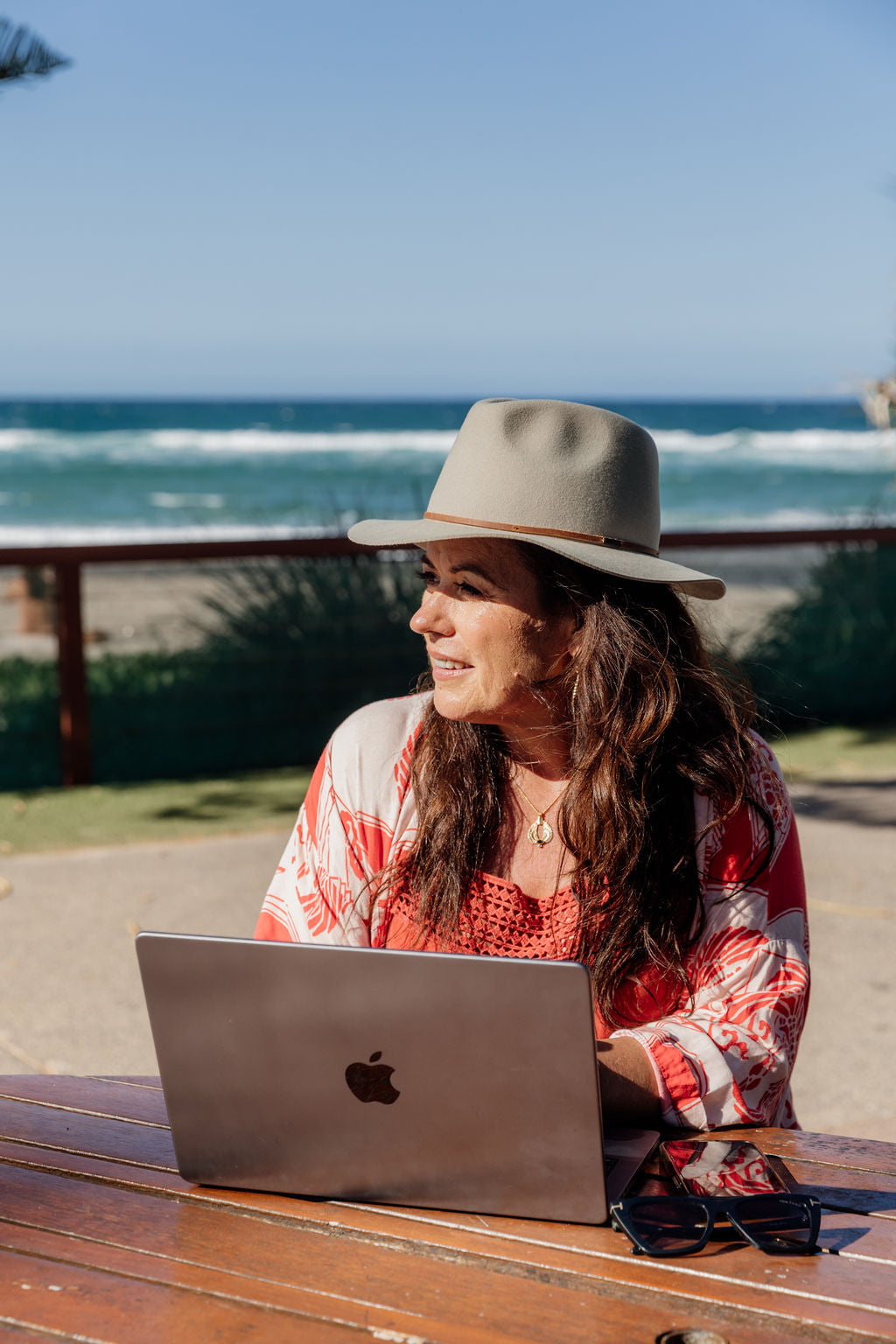 Penny Locaso sitting at table by the beach working on a laptop