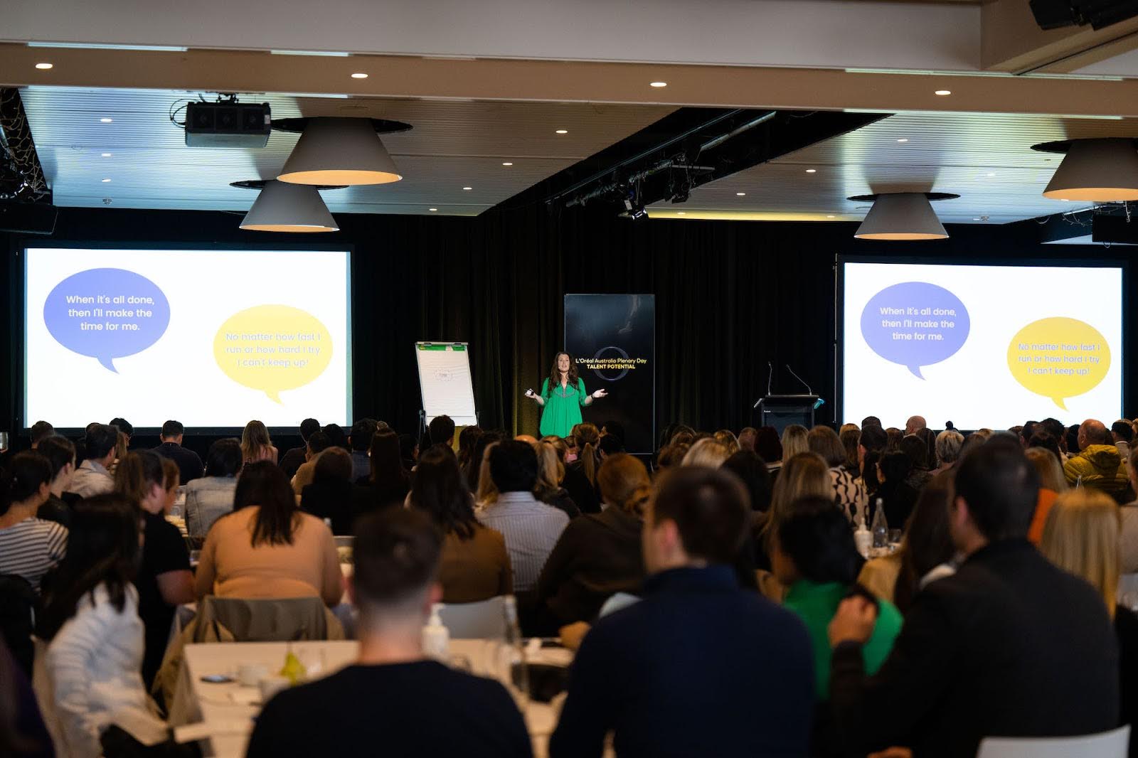 Woman in green dress speaking on a stage in front of audience