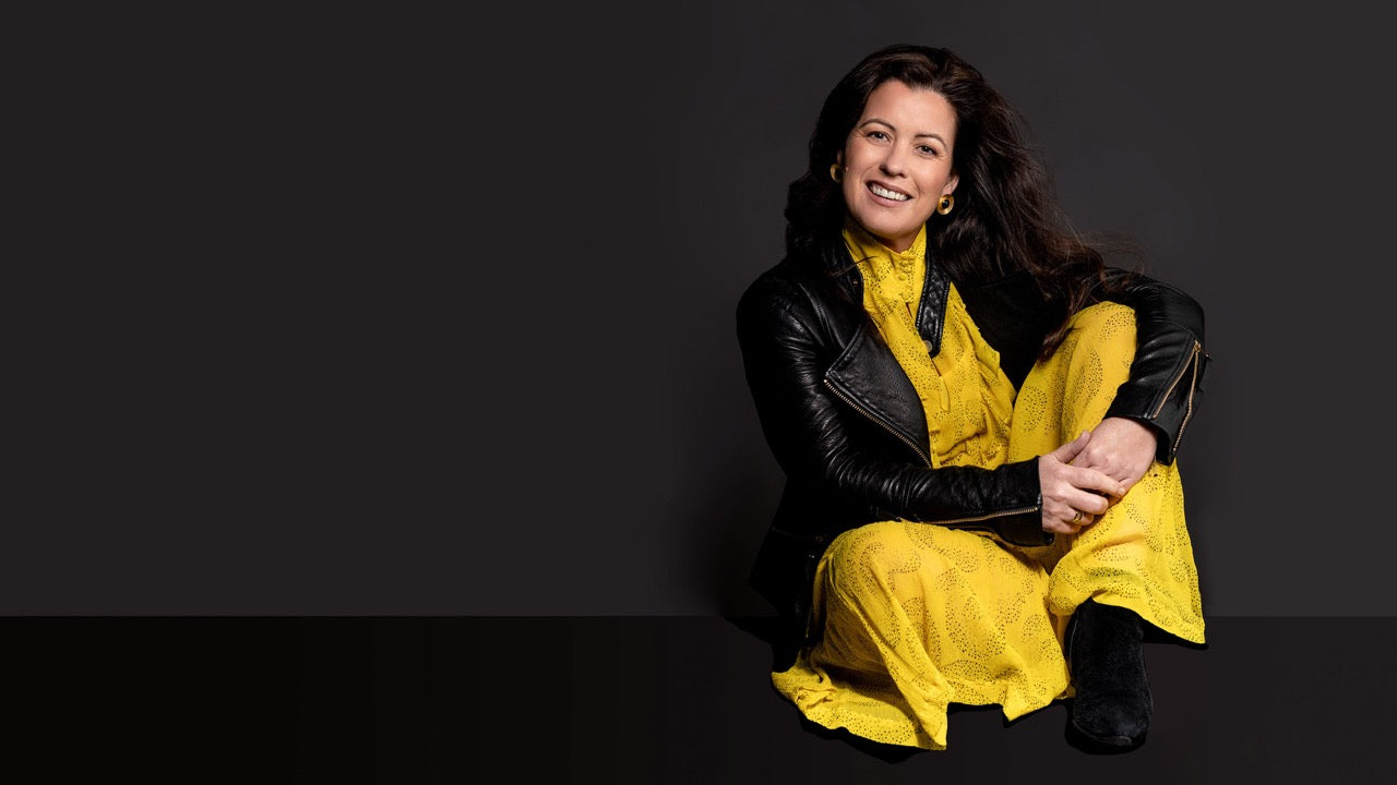 Woman sitting down in a yellow dress and black leather jacket