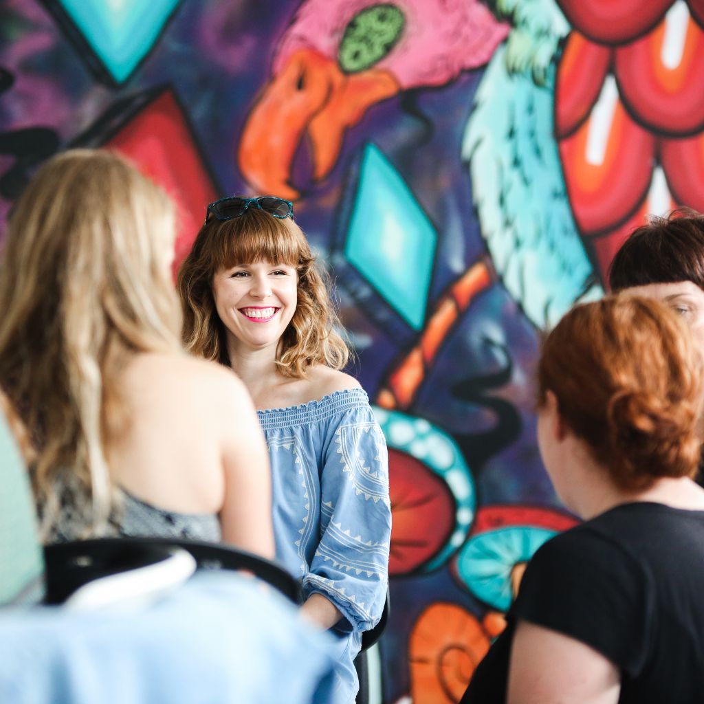 Female participants in a workshop sit in front of a graffiti wall.