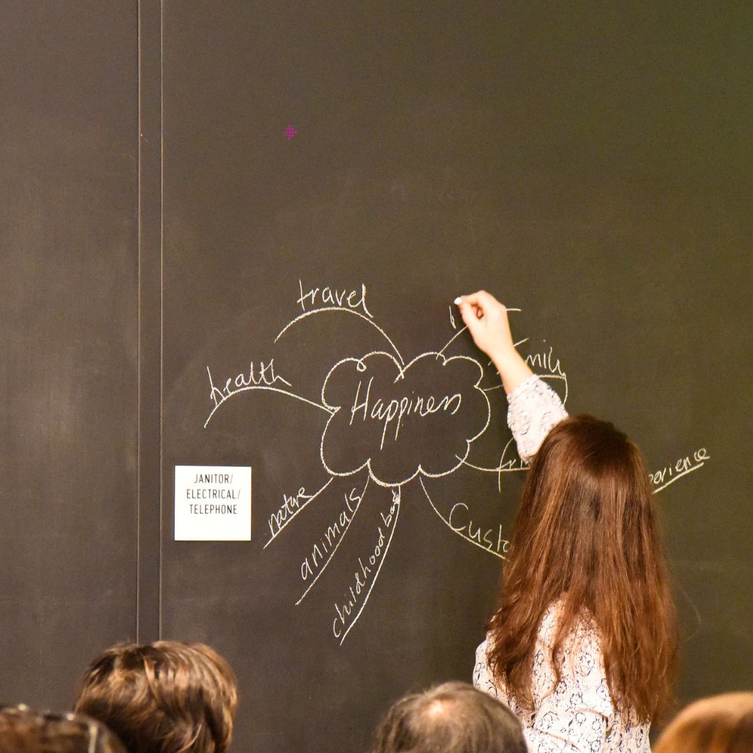 A woman is drawing a cloud diagram on a chalkboard in front of a classroom.