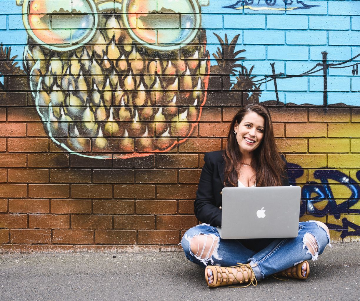 Woman working on her laptop while sitting in front of a graffiti wall.