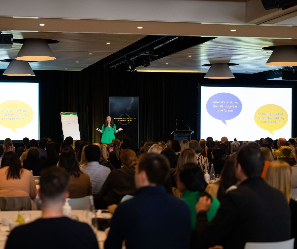 Woman is giving a presentation on stage to a corporate audience.
