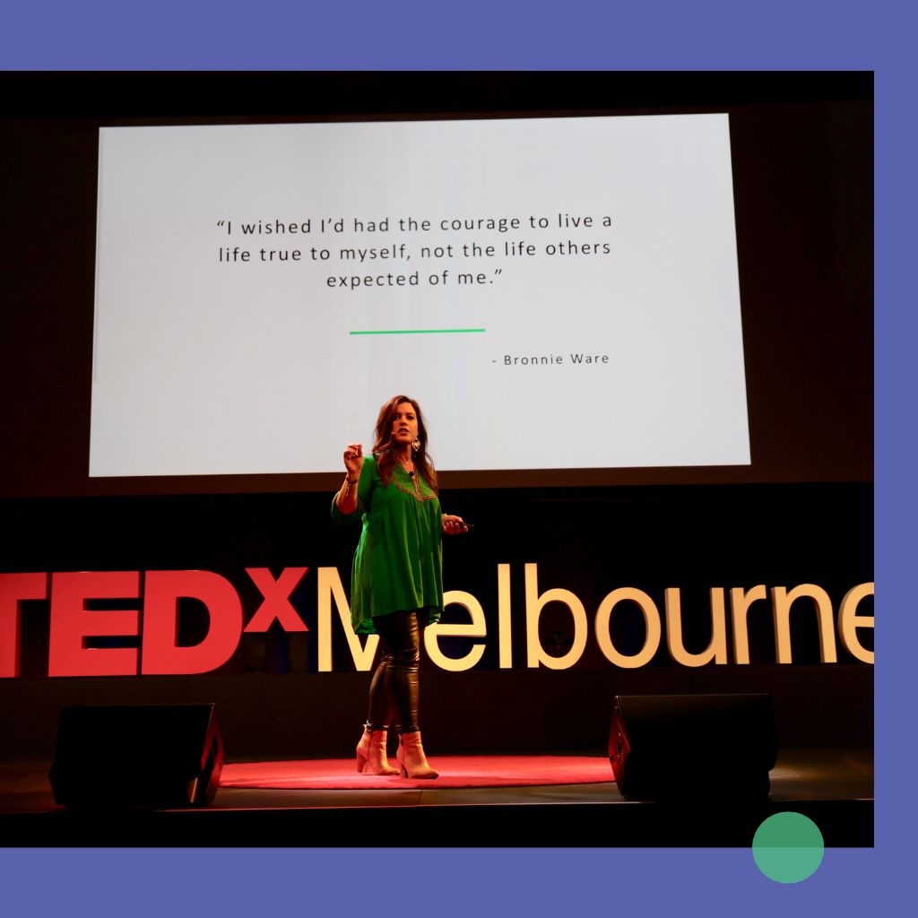 Woman speaking on TEDx Melbourne stage with a big screen presentation slide behind her.