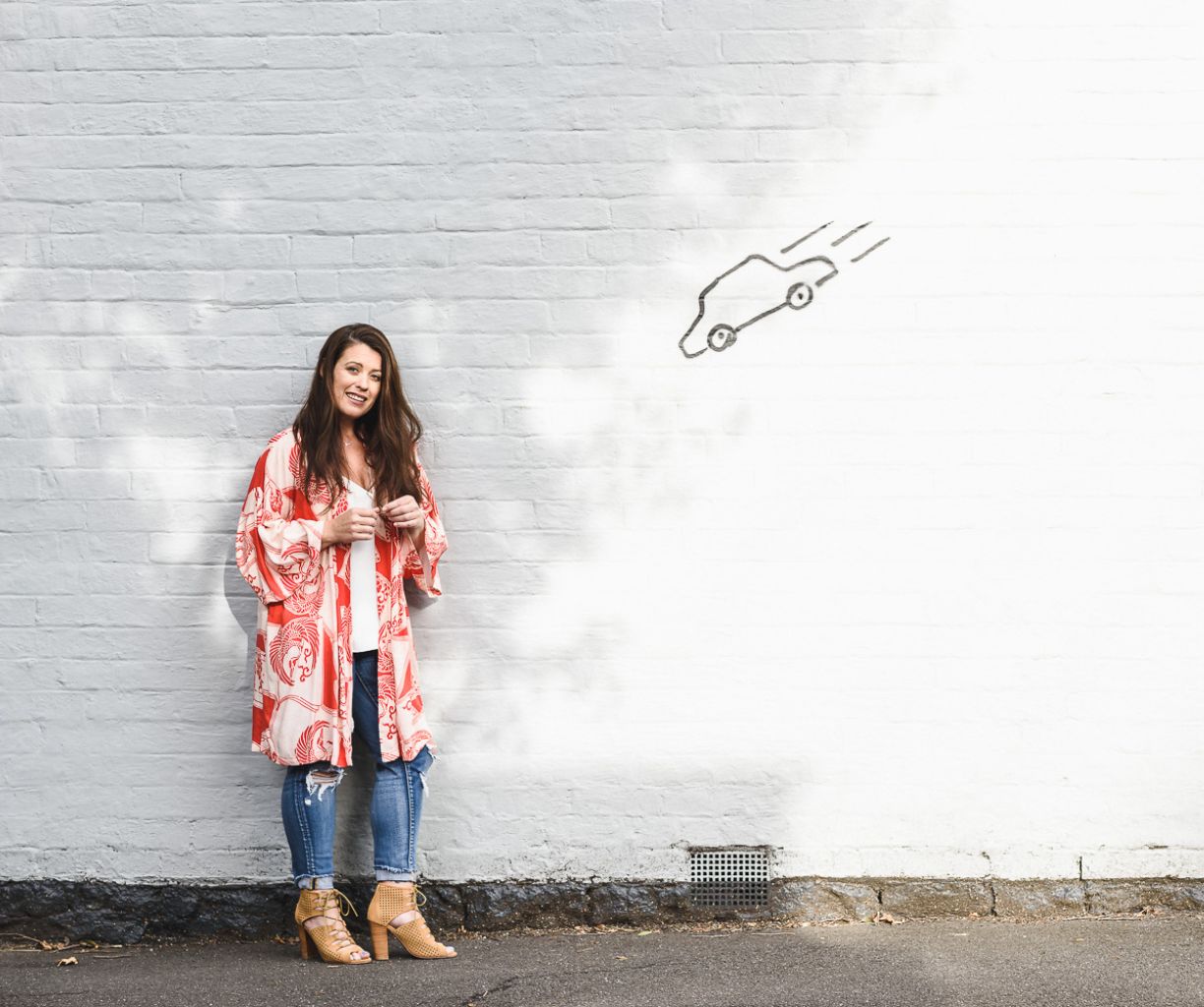 Woman is standing in front of a white brick wall with car graffiti. 